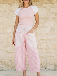 Woman wearing a pastel pink and white outfit against a stone wall.