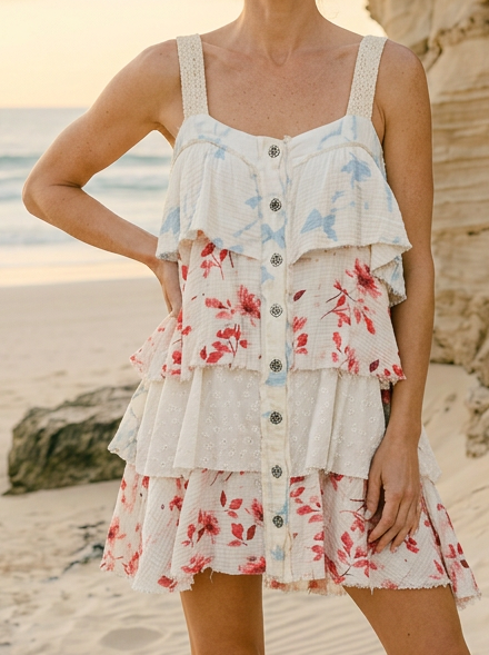 Woman in a floral dress standing on a beach with sunset and rocks in the background