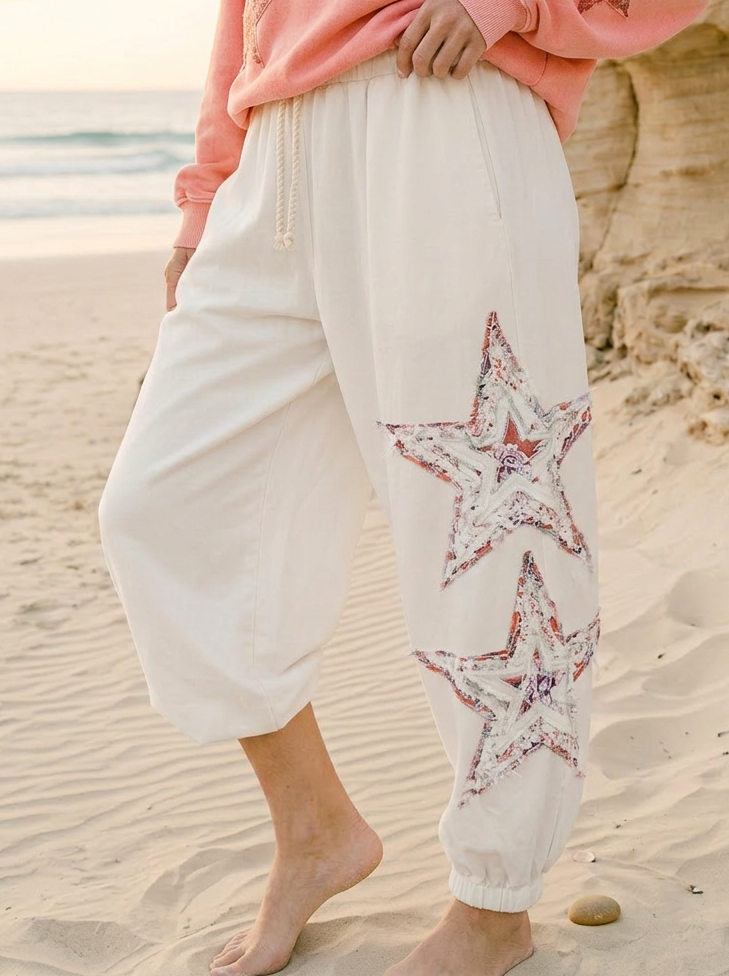 Person wearing a pink sweatshirt and white pants with star patterns on a beach.