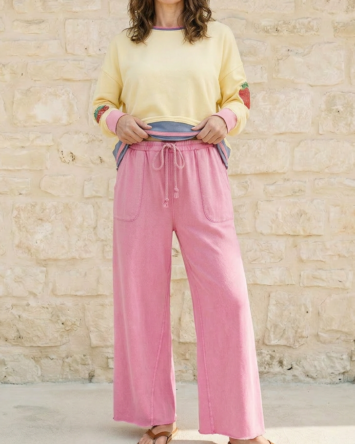 Woman wearing a yellow sweater and pink pants standing against a stone wall.
