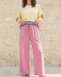 Woman wearing a yellow sweater and pink pants standing against a stone wall.