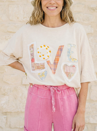 Woman wearing a colorful 'LOVE' sweater and pink pants against a stone wall.