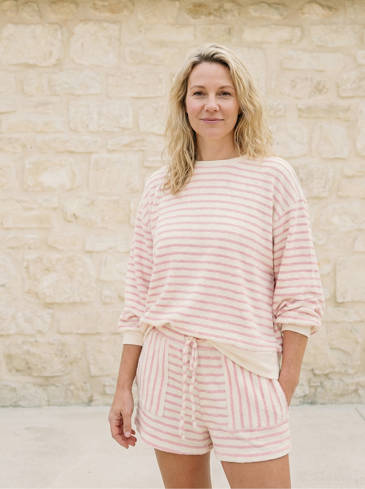Woman wearing a pink striped outfit standing against a stone wall.